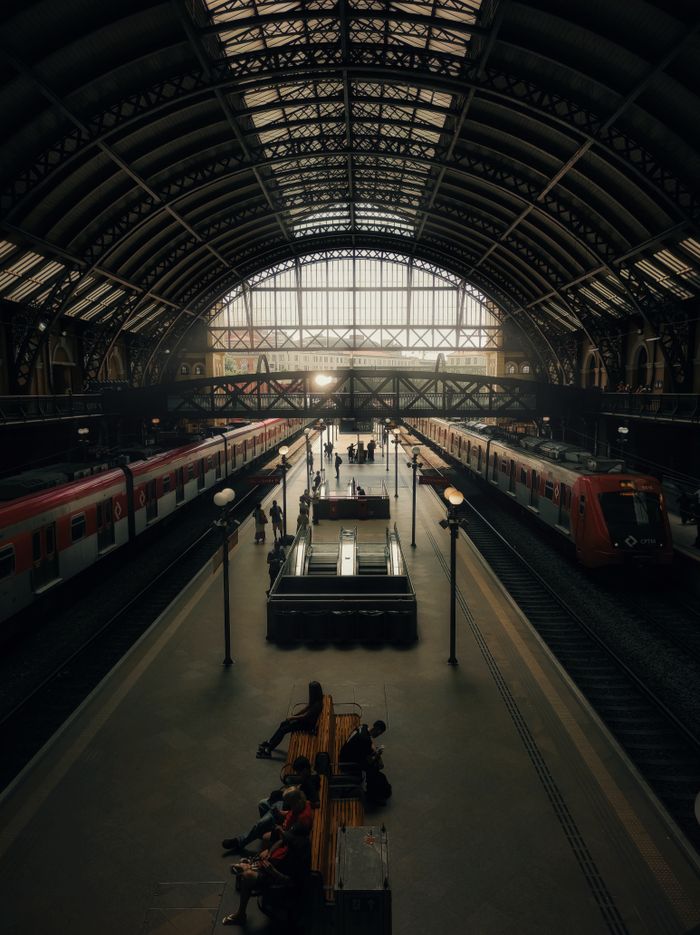 why-choose-us High-angle view of São Paulo train station with commuters and trains under a grand arched roof.